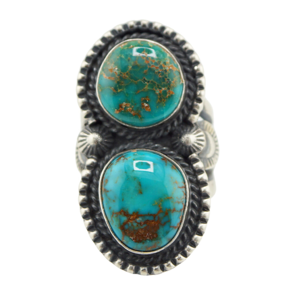 The “Twin Spirits” Revival Ring by Derrick Gordon (Navajo) features two oval turquoise stones with brown matrix, set vertically in silver with beaded edges and leaf-like side accents.