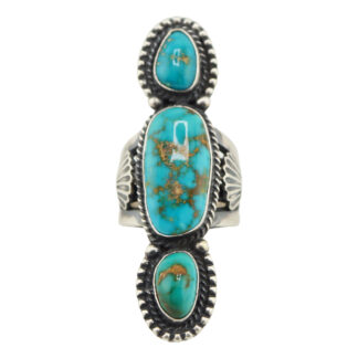 The “Twin Spirits” Revival Ring by Derrick Gordon (Navajo) is a silver ring with three vertically set oval turquoise stones showing brown veining, each bordered by intricate silverwork.