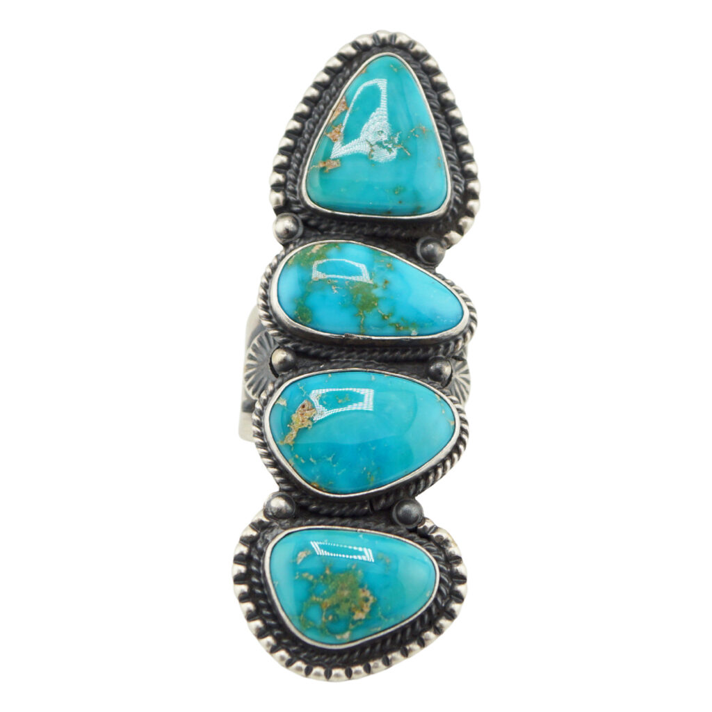 The “Twin Spirits” Revival Ring by Derrick Gordon (Navajo) is a silver ring with four oval and teardrop turquoise stones set in decorative bezels with rope-like edges, arranged vertically down the band.