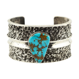 The Royston Ridge Cuff by Lester James (Navajo) features a wide, textured silver band with a central teardrop turquoise stone showcasing brown and gold matrix, accented by a raised horizontal silver band.