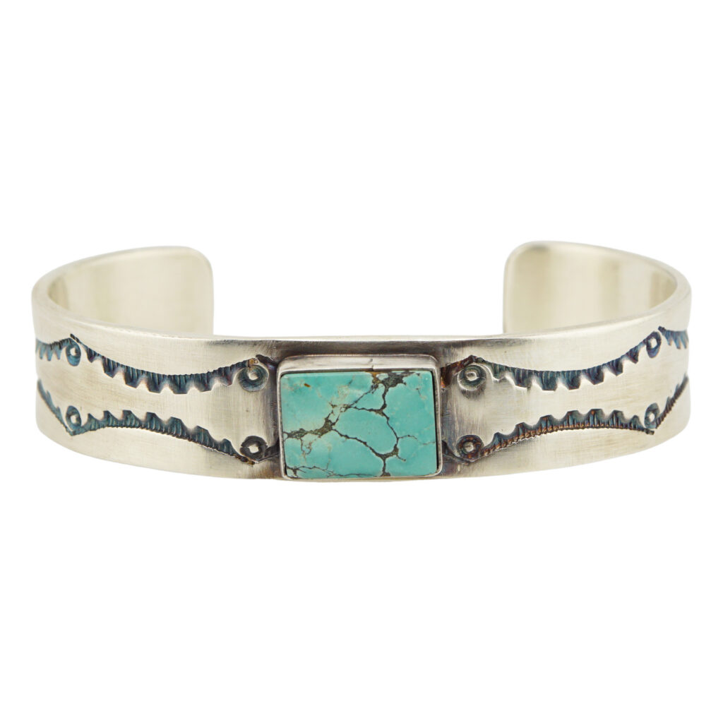 The Chinese Turquoise Stamped Cuff by Melvin Francis (Navajo) is a silver bracelet with a central rectangular turquoise stone featuring black veining and engraved patterns flanking the stone.