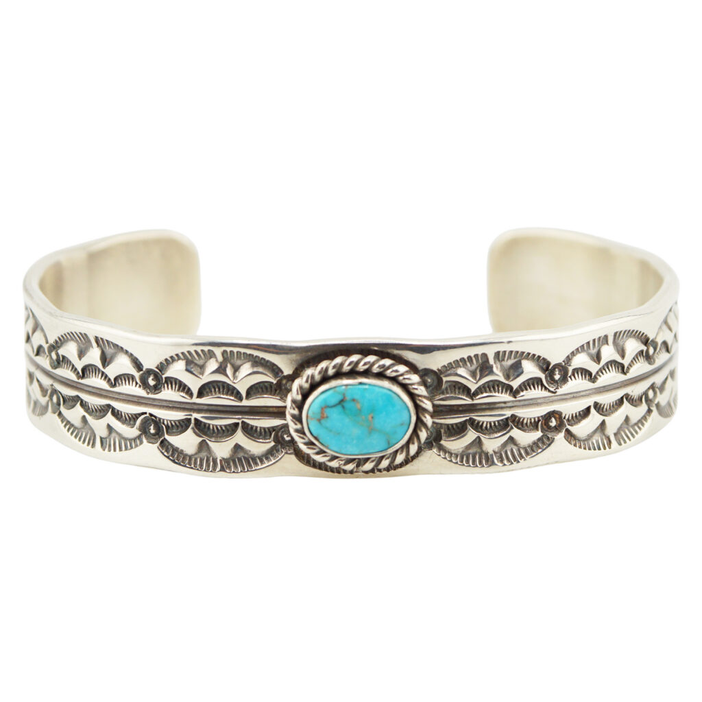 A silver cuff bracelet with intricate engraved patterns and a central oval turquoise stone set in a twisted rope design.