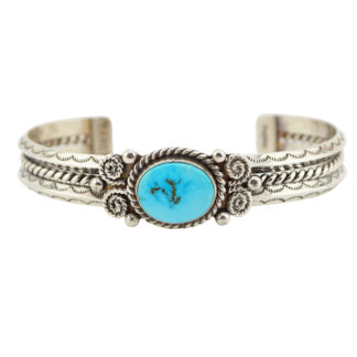 A silver cuff bracelet featuring intricate braided and twisted designs, with a central oval turquoise stone set in an ornate bezel.