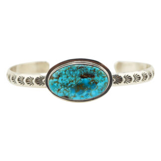 A silver cuff bracelet with an engraved pattern featuring a large oval turquoise stone with black veining set in the center.