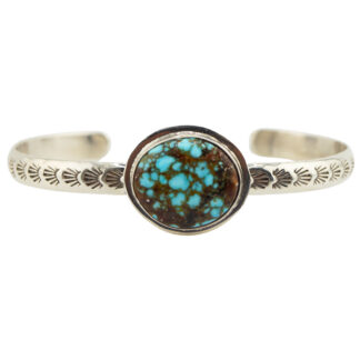 A silver cuff bracelet with engraved patterns and a large, round turquoise stone featuring brown matrix in the center.