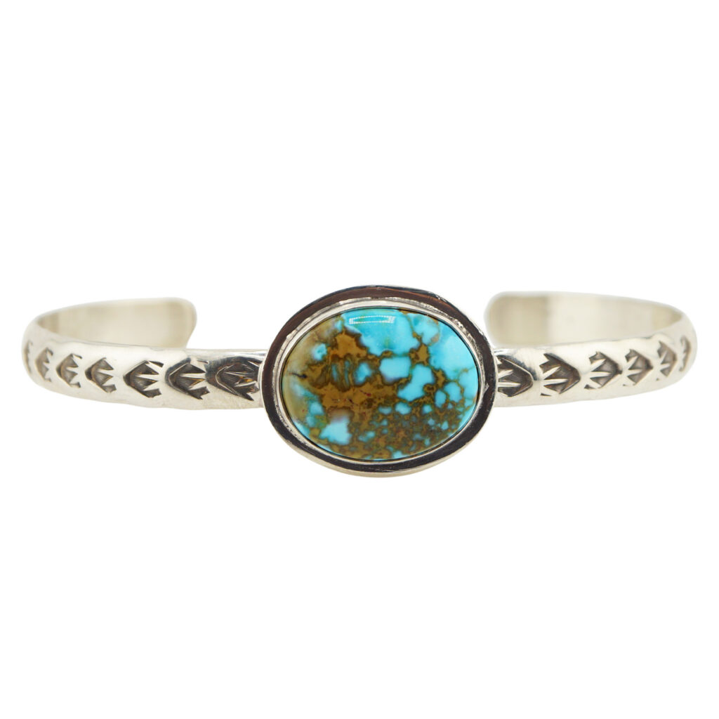 A silver cuff bracelet features engraved arrow patterns and a central oval turquoise stone with a brown matrix.