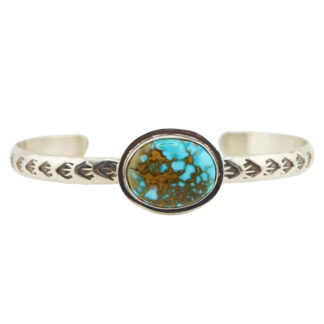 A silver cuff bracelet features engraved arrow patterns and a central oval turquoise stone with a brown matrix.