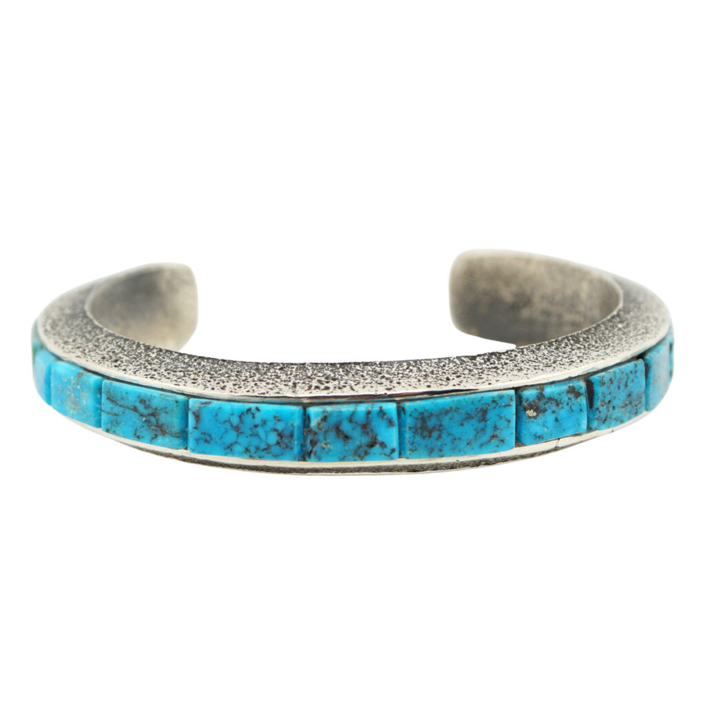 A silver cuff bracelet featuring a row of rectangular turquoise stones with black veining, set along the outer edge. The bracelet has a slightly textured surface and an open back.
