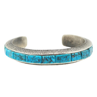 A silver cuff bracelet featuring a row of rectangular turquoise stones with black veining, set along the outer edge. The bracelet has a slightly textured surface and an open back.