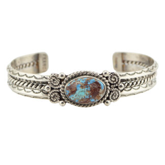 A silver cuff bracelet featuring an oval turquoise stone with brown and blue patterns, detailed with intricate engraved designs and twisted rope accents on both sides.