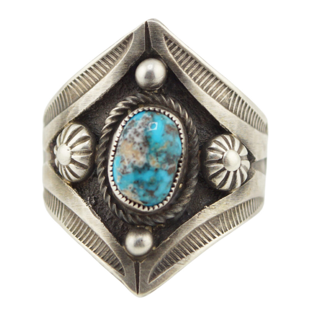 Silver ring with engraved geometric patterns, featuring a central oval turquoise stone surrounded by silver accents and decorative etching.