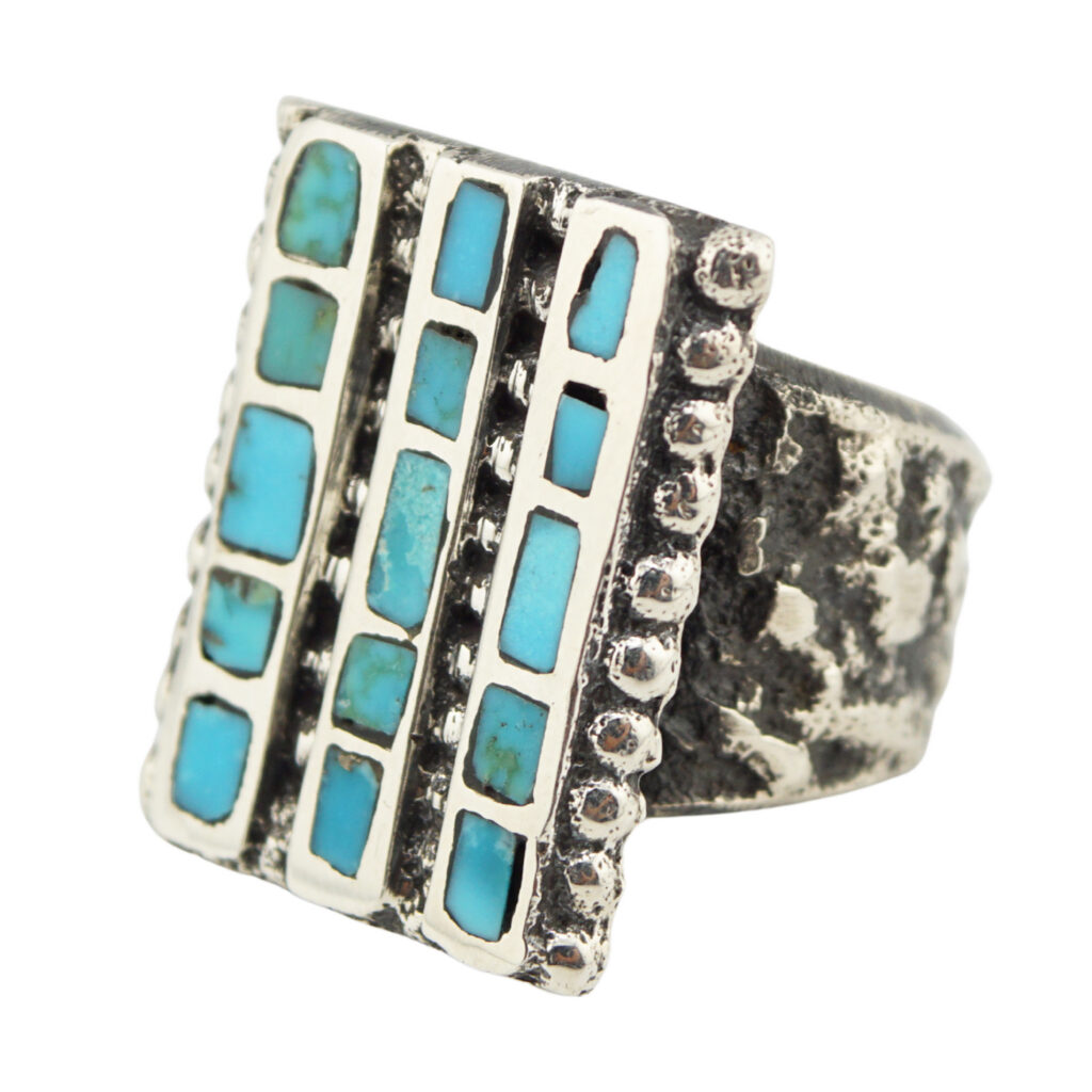 A silver ring with a wide, textured band and a rectangular face featuring vertical rows of turquoise inlays set in a geometric pattern.