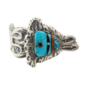 A silver ring featuring a fish-shaped design with inlaid turquoise, black, white, and brown stones forming the fishs face and body details. The band has a textured, organic pattern.