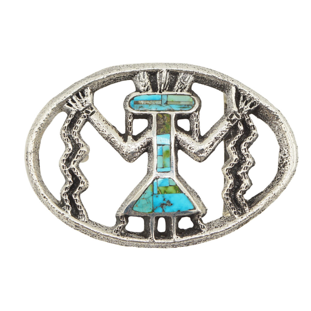 Oval-shaped silver belt buckle featuring a stylized figure with raised arms, turquoise and green stone inlays, and zigzag lines on each side, resembling Southwestern or Native American design.