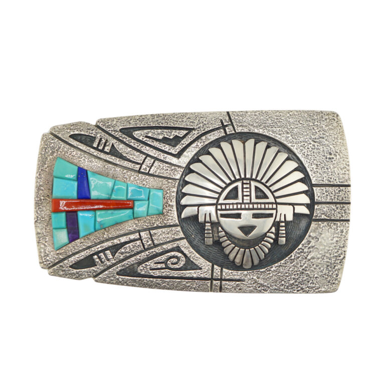 A silver belt buckle features a raised geometric sunface design on the right and turquoise, red, and blue inlaid stones forming an abstract cross pattern on the left, with textured and patterned detailing throughout.
