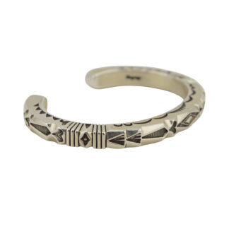 A silver cuff bracelet with intricate engraved geometric patterns, featuring triangles, lines, and diamond shapes. The bracelet is open-ended and has a polished, metallic finish.