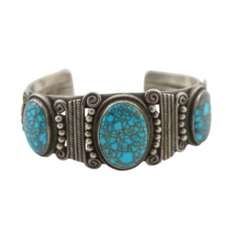 A silver cuff bracelet featuring three large oval turquoise stones with intricate metalwork, including swirls and bead accents, surrounding the stones.